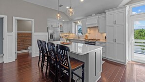 A spacious kitchen with a large island, white cabinetry, and a view of greenery outside. - 4919-The Leonardo - Soundside Oasis | Pool, Hot Tub & Fire Pit (Kitty Hawk)