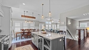 A spacious kitchen with a central island, wooden dining table, and pendant lighting. - 4919-The Leonardo - Soundside Oasis | Pool, Hot Tub & Fire Pit (Kitty Hawk)