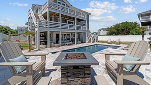 A two-story house with a pool, outdoor seating, and a stone fire pit. - 4919-The Leonardo - Soundside Oasis | Pool, Hot Tub & Fire Pit (Kitty Hawk)