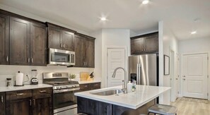 A modern kitchen with dark wood cabinets, stainless steel appliances, and a central island with stools.