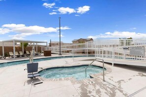 A pool area with a hot tub, lounge chairs, and a covered seating area.