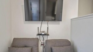 A room with a mounted flat-screen TV, a small shelf with electronic devices, and two grey armchairs. - Ideal Family Getaway- Pickleball, Pool & Near Zion (Washington)