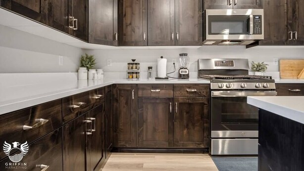 A modern kitchen with dark wood cabinets, stainless steel appliances, and a white countertop. - Ideal Family Getaway- Pickleball, Pool & Near Zion (Washington)