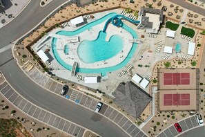 Vista aérea de un complejo turístico con piscina central, canchas de tenis y un estacionamiento.