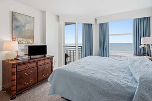 Una habitación de hotel con cama, cómoda, televisor y un cuadro.
