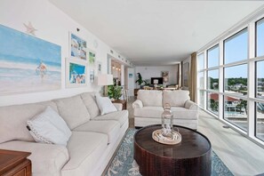 A spacious living room with a large window, a sofa, a coffee table, and a dining area.
