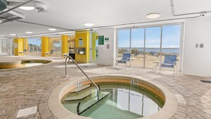 Una piscina interior con un indicador de profundidad de 3 pies, rodeada de sillas de descanso y vistas a la playa a través de amplias ventanas.