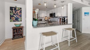 Una cocina moderna con armarios blancos, encimera de granito e iluminación colgante.