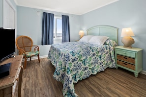 Une chambre à coucher comprenant un lit, une chaise, une table de chevet, une lampe et un téléviseur.