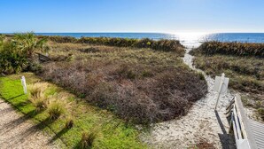 A beach path leading to the ocean, surrounded by vegetation and a wooden boardwalk. - Stunning views, stylish oceanfront condo close to nightlife, shopping, dining and more! (North Myrtle Beach)