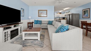 A modern living room with a flat-screen TV, a white sofa, a coffee table, and a dining area with a wooden table and chairs. - Spacious 5 bedroom oceanview condo - Cherry Grove Beach (North Myrtle Beach)