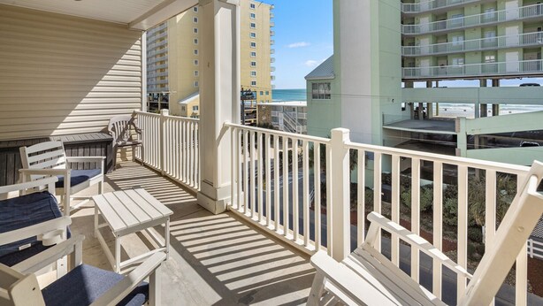A balcony with white railings, wooden furniture, and a view of a beach and buildings. - Spacious 5 bedroom oceanview condo - Cherry Grove Beach (North Myrtle Beach)