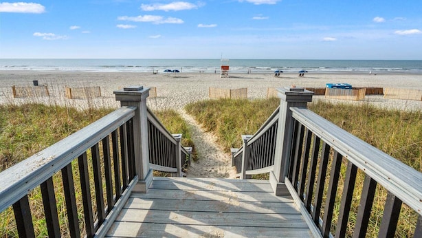 Une promenade en bois qui mène à une plage, avec un ciel dégagé.