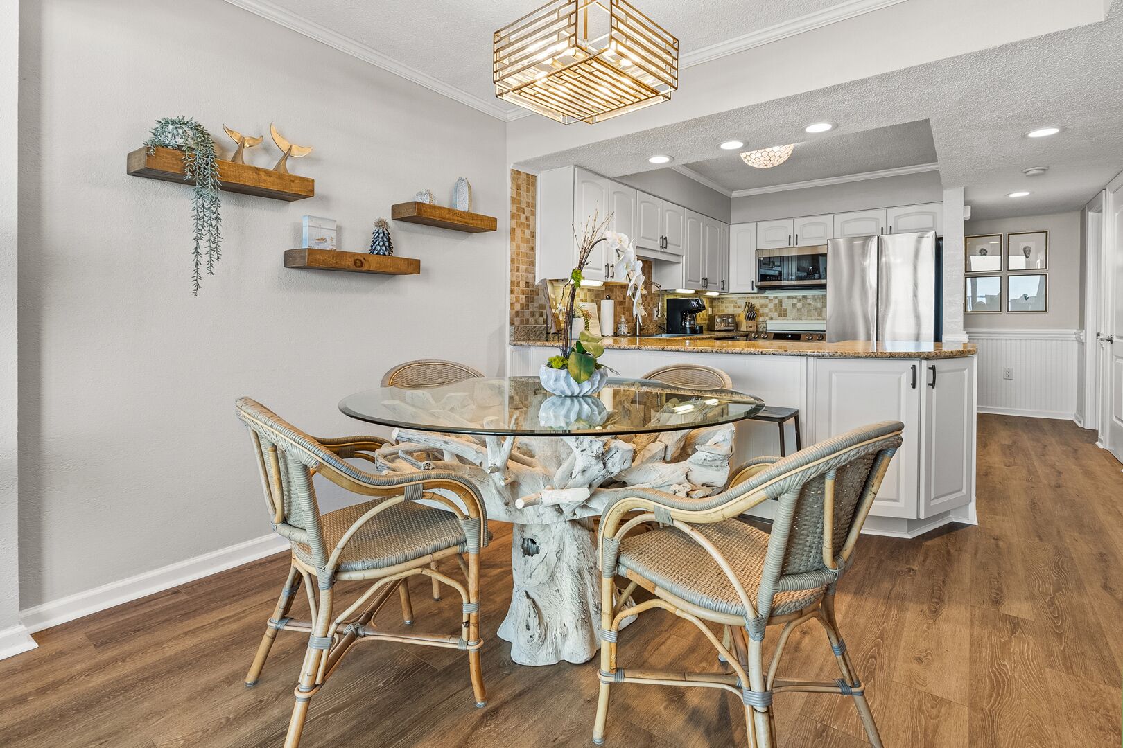 A modern kitchen with white cabinets, a stainless steel refrigerator, and a dining area with wicker chairs and a glass table.