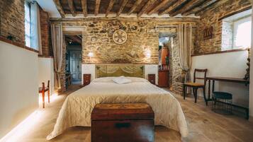 Una camera da letto rustica con parete in pietra, travi in legno, un letto, un comò e una scrivania.