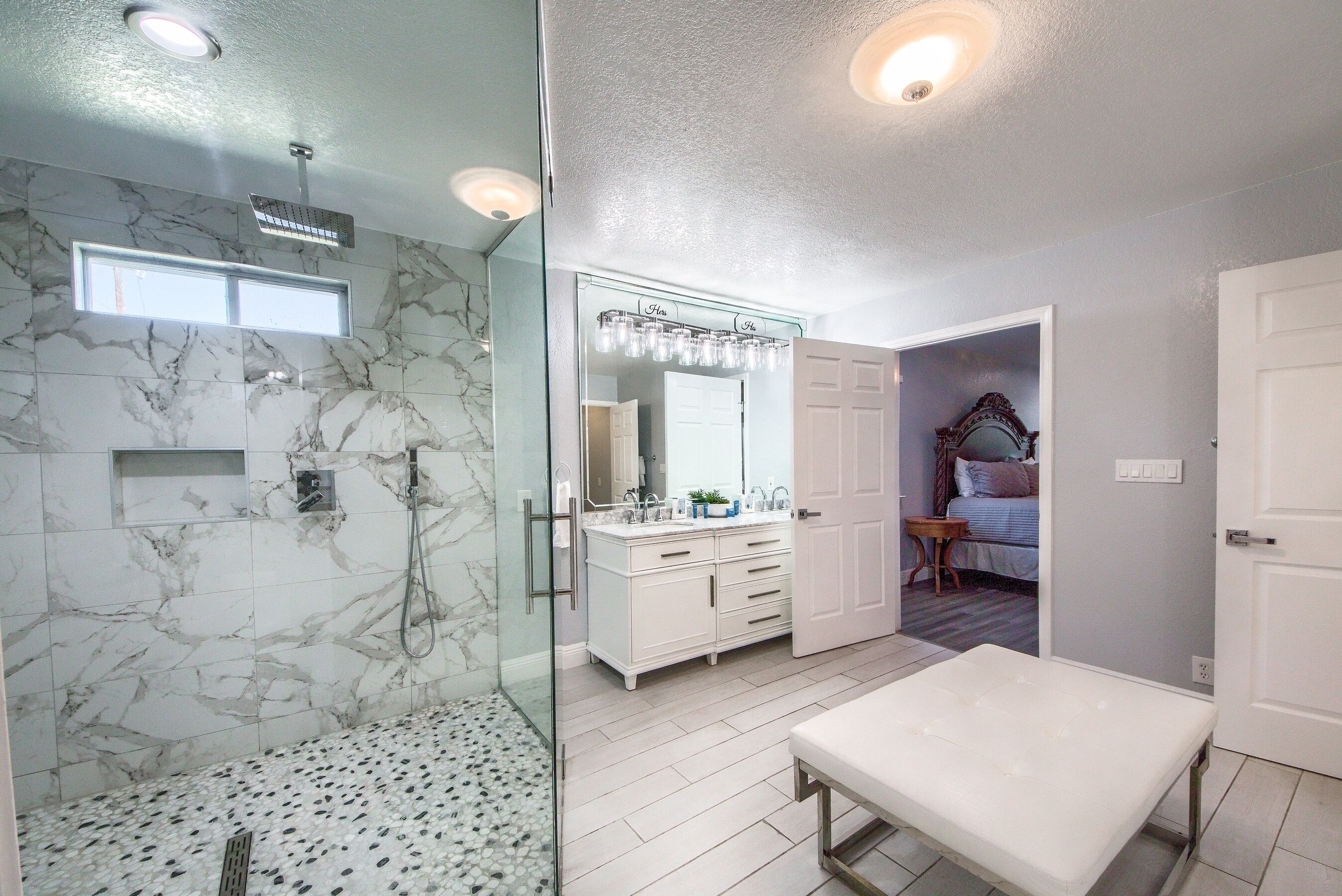 A bathroom with a glass-enclosed shower, marble walls, a vanity with a mirror, and a bench.