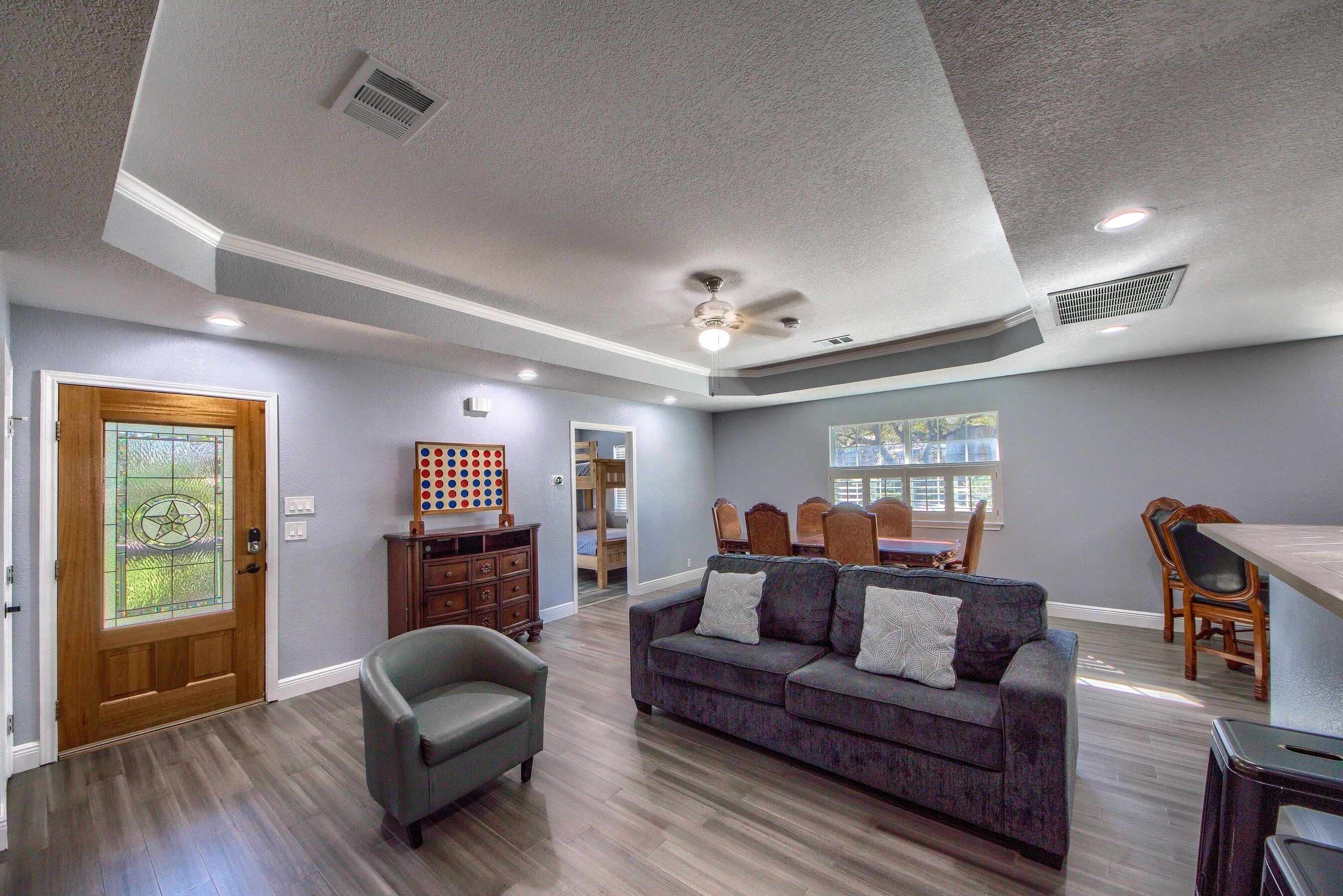 A spacious living room with a gray couch, wooden floor, and a dining area with chairs and a table.