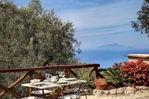 An outdoor dining area with a table set for two, overlooking a scenic view of the sea and mountains. - Tulipano - A Charming and Peaceful Hillside Villa With Lovely Views (Massa Lubrense)