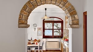 A kitchen with a stone archway, a window with a view of trees, and a dining area with chairs and a table set with food and drinks. - Tulipano - A Charming and Peaceful Hillside Villa With Lovely Views (Massa Lubrense)