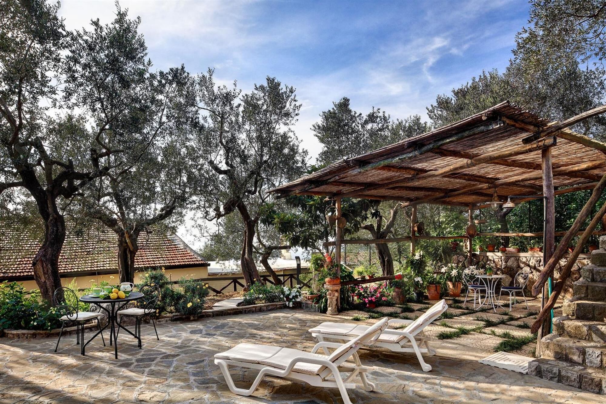 Une terrasse en pierre avec des chaises longues, une table et une pergola.