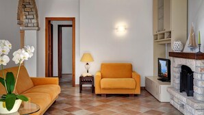 A living room with a sofa, a small table with a lamp, a television, and a fireplace. - Tulipano - A Charming and Peaceful Hillside Villa With Lovely Views (Massa Lubrense)