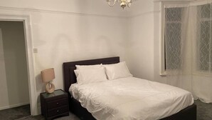 A bedroom with a bed, bedside table, lamp, and a chandelier.
