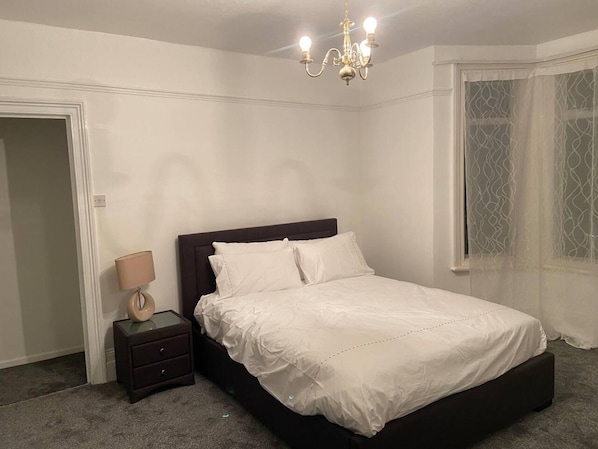 A bedroom with a bed, bedside table, lamp, and a chandelier.
