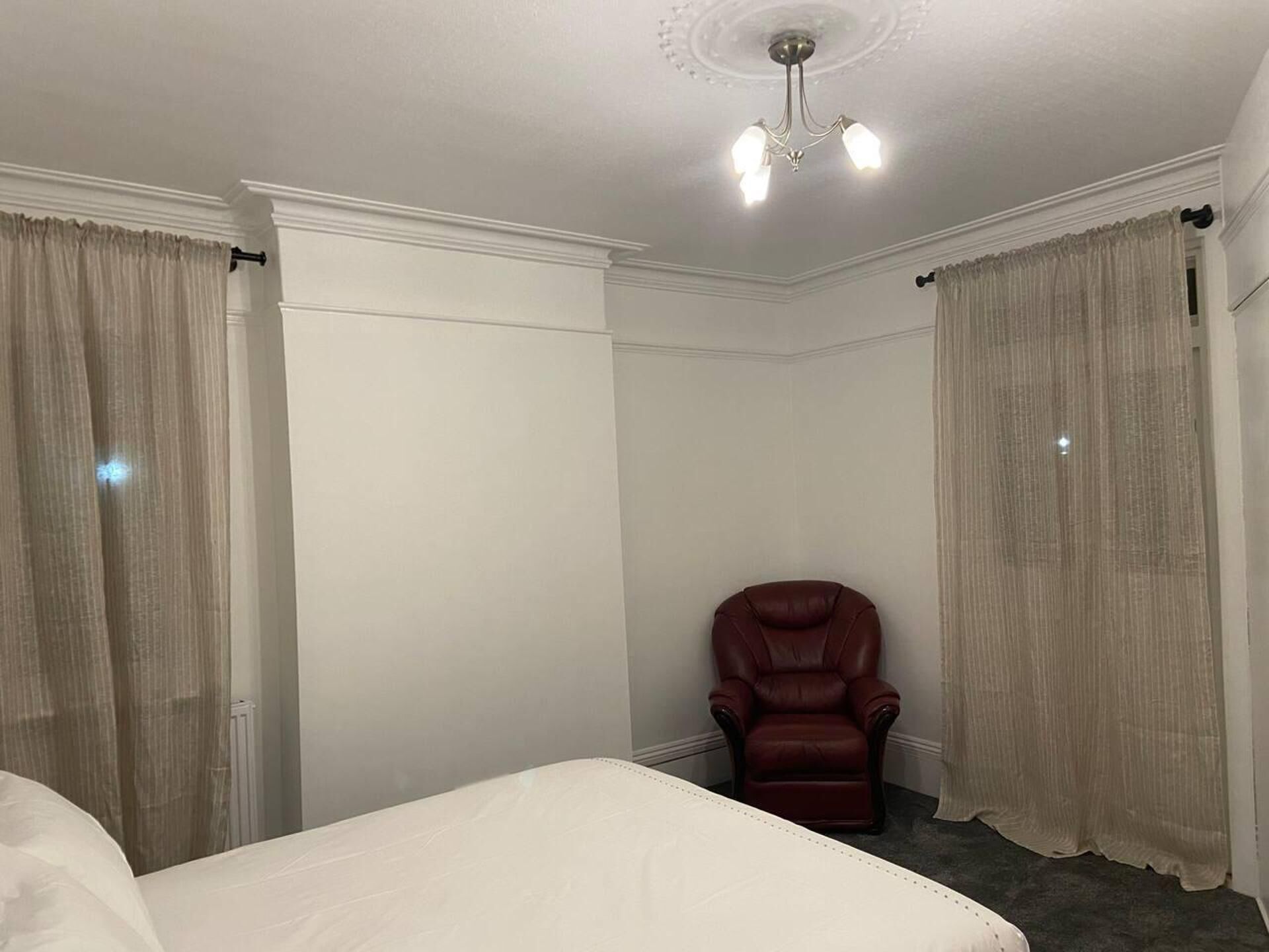 A hotel room with a large bed, a leather armchair, and beige curtains.