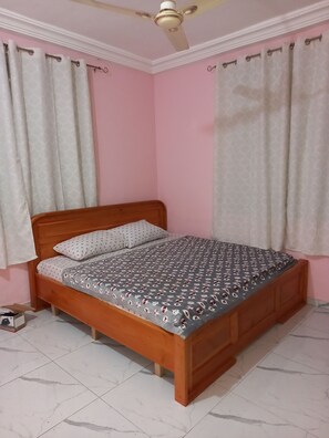 Un dormitorio con cama de madera, ropa de cama estampada y ventilador de techo.