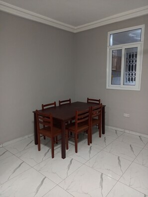 Comedor con mesa rectangular y seis sillas, ventana con rejas y piso de baldosas blancas.