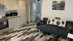 A modern kitchen with white cabinets, a microwave, and a toaster. There is a dark-colored sofa with decorative pillows and a painting on the wall. - Impeccable 1-bed Apartment in Chesterfield (Chesterfield)