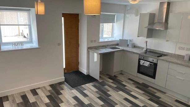 A modern kitchen with a built-in oven, a dishwasher, and a sink. There are pendant lights and a window providing natural light. - Impeccable 1-bed Apartment in Chesterfield (Chesterfield)