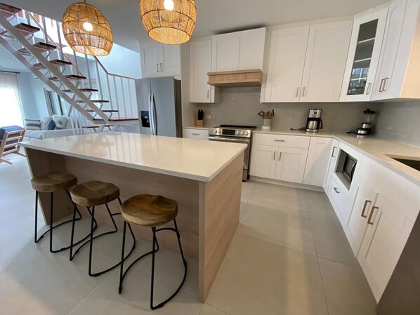 Una cocina moderna con una isla grande, armarios blancos y una escalera que lleva a un dormitorio tipo loft.