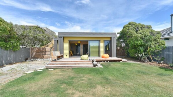 Una casa moderna con jardín delantero, terraza de madera y un árbol grande.