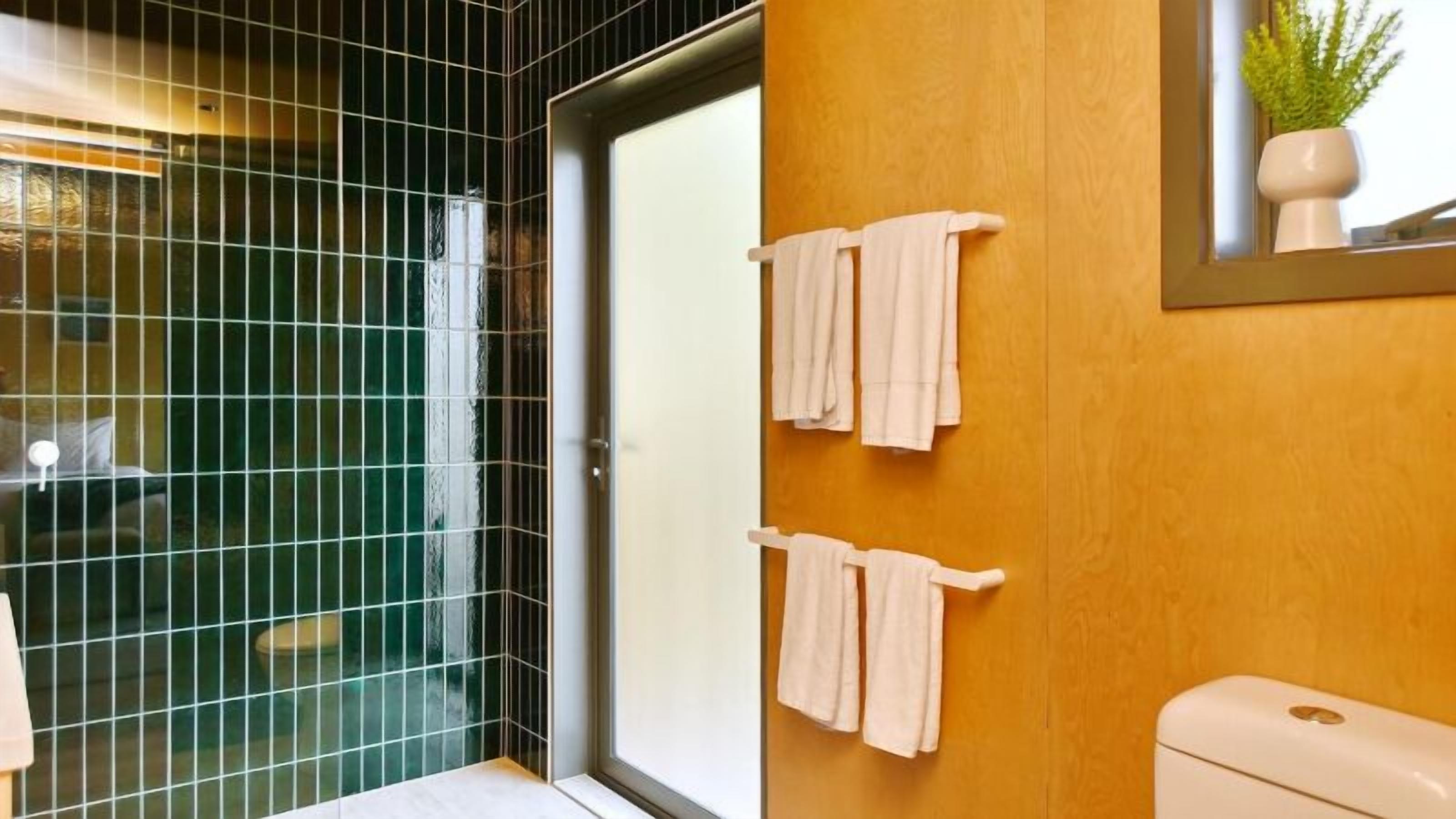 A bathroom with a green-tiled shower area, wooden wall paneling, and a toilet with a white lid.