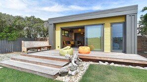 Una casa moderna con fachada amarilla, una terraza con escalones que conducen a una puerta de cristal y mobiliario exterior.