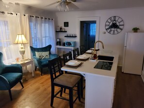 Un espace de vie compact comprenant un coin cuisine, un coin repas et un espace détente avec un canapé et des fauteuils.