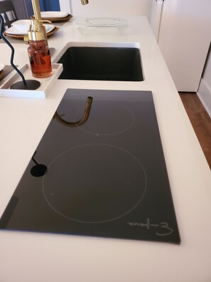 Une cuisine dotée d’une plaque de cuisson à induction noire, d’un plan de travail blanc et d’un distributeur d’eau en verre.