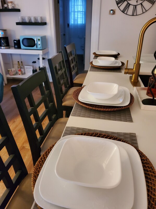 Un coin repas avec une table blanche dressée pour quatre personnes, comprenant des assiettes, des bols et un robinet doré.