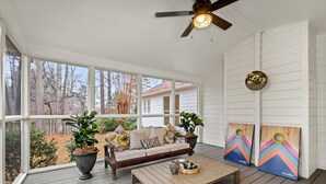 A covered porch with a sofa, coffee table, and two decorative boards. - Renovated Ranch Home. Pet Friendly, Game Room, Fire Pit, Grill, Covered Porch (Woodstock)