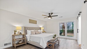 A bedroom with a bed, bedside tables, a bench, a ceiling fan, and a large window. - Renovated Ranch Home. Pet Friendly, Game Room, Fire Pit, Grill, Covered Porch (Woodstock)