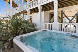 A hot tub with a wooden deck and railing, surrounded by palm plants.