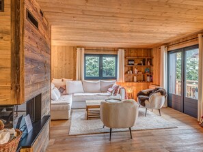 Interior acogedor de una cabaña de madera con sofá, sillones, chimenea y estantería.