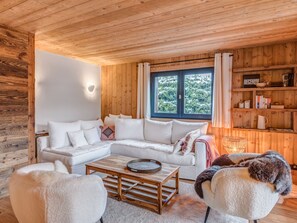 Interior acogedor de una cabaña con techo de madera, un sofá blanco, una mesita de centro y una estantería.
