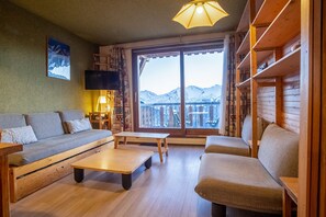 Een gezellige woonkamer met een bank, een salontafel en een televisie. Een groot raam biedt uitzicht op bergen.