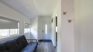 Ein Flur mit grauem Sofa, einer weißen Tür mit Fenster und Wanddekorationen mit Schmetterlingsmotiven.
