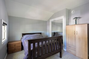 Une chambre avec un lit en bois, une armoire, une commode et une fenêtre.