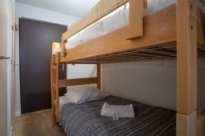 A bunk bed room with a dark door, a small bedside table, and a patterned bedspread.