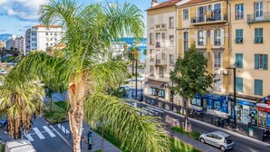 A street view with a row of buildings, palm trees, and parked cars. - Appartement California - Welkeys (Nice)