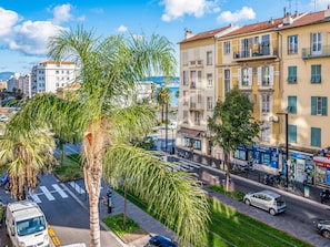 Vista de una calle con edificios, palmeras y coches estacionados.